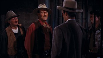 Movie still from “Rio Bravo” (1959), directed by Howard Hawks – A man in a cowboy hat talking to another man in a suit; Medium shot, Over the shoulder angle