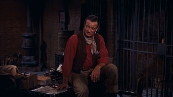 Movie still from “Rio Bravo” (1959), directed by Howard Hawks – A man sitting on top of a chair in front of a fire place; Medium shot, High angle