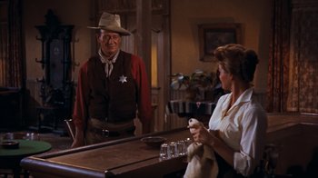 Movie still from “Rio Bravo” (1959), directed by Howard Hawks – A man and a woman are standing at a bar; Medium shot, Over the shoulder angle
