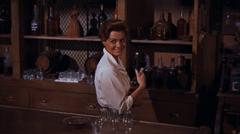 Movie still from “Rio Bravo” (1959), directed by Howard Hawks – A woman sitting at a bar holding a glass; Medium shot, Low angle