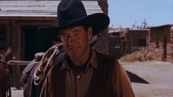 Movie still from “Rio Bravo” (1959), directed by Howard Hawks – A man wearing a cowboy hat standing in front of a building; Close Up shot, Over the shoulder angle