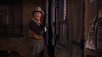 Movie still from “Rio Bravo” (1959), directed by Howard Hawks – An older man in a hat and vest standing in a doorway; Medium shot, Low angle