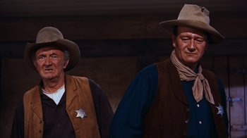 Movie still from “Rio Bravo” (1959), directed by Howard Hawks – A couple of men standing next to each other wearing hats; Medium shot, Low angle
