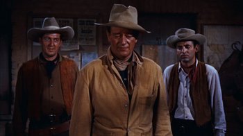 Movie still from “Rio Bravo” (1959), directed by Howard Hawks – A man in a cowboy hat standing next to two other men; Medium shot, Low angle