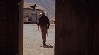 Movie still from “Rio Bravo” (1959), directed by Howard Hawks – A man in a cowboy hat is holding a gun; Wide shot, Low angle