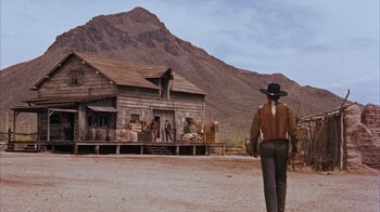 Movie still from “Rio Bravo” (1959), directed by Howard Hawks – A man standing in front of an old house on the side of a dirt road; Extreme Wide shot, Low angle