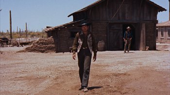 Movie still from “Rio Bravo” (1959), directed by Howard Hawks – A man in a cowboy hat walking in a dirt field; Wide shot, Low angle