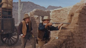 Movie still from “Rio Bravo” (1959), directed by Howard Hawks – Two men in cowboy hats are shooting a gun; Medium shot, Over the shoulder angle