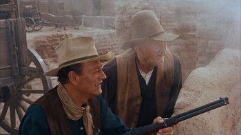 Movie still from “Rio Bravo” (1959), directed by Howard Hawks – A couple of men sitting next to each other holding a gun; Medium shot, Over the shoulder angle