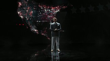 Movie still from “RoboCop” (2014), directed by José Padilha – A man standing in front of an image of the american flag; Wide shot, High angle