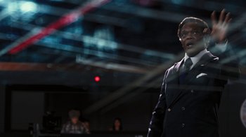 Movie still from “RoboCop” (2014), directed by José Padilha – A man wearing a suit and tie standing in front of a crowd; Medium shot, Over the shoulder angle