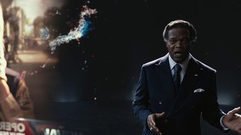 Movie still from “RoboCop” (2014), directed by José Padilha – A man wearing a suit and tie standing in front of a black background; Medium shot, Over the shoulder angle