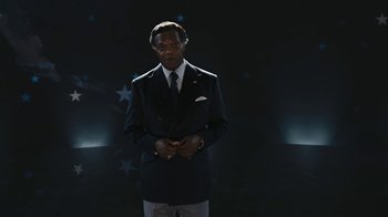 Movie still from “RoboCop” (2014), directed by José Padilha – A man in a suit and tie standing in front of a wall; Medium shot, Low angle