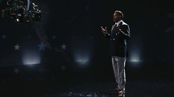 Movie still from “RoboCop” (2014), directed by José Padilha – A man standing on a stage in front of a camera; Wide shot, Low angle