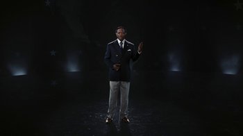 Movie still from “RoboCop” (2014), directed by José Padilha – A man standing in a dark room wearing a suit and tie; Medium shot, Low angle