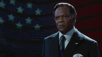 Movie still from “RoboCop” (2014), directed by José Padilha – A man in a suit and tie standing in front of a flag; Close Up shot, Low angle