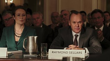 Movie still from “RoboCop” (2014), directed by José Padilha – A man sitting at a table in front of a group of people; Medium shot, Over the shoulder angle