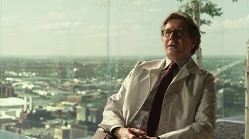 Movie still from “RoboCop” (2014), directed by José Padilha – An older man wearing a white coat and a red tie; Medium shot, Low angle