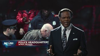 Movie still from “RoboCop” (2014), directed by José Padilha – A man in a suit and tie standing in front of a tv; Close Up shot, Over the shoulder angle