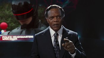Movie still from “RoboCop” (2014), directed by José Padilha – A man in a suit and tie pointing at the camera; Close Up shot, Over the shoulder angle