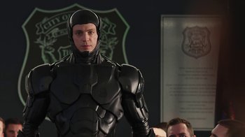 Movie still from “RoboCop” (2014), directed by José Padilha – A man in a black suit standing in front of other people; Medium shot, Low angle