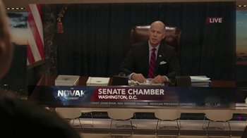 Movie still from “RoboCop” (2014), directed by José Padilha – A man sitting at a desk in front of a microphone; Medium shot, Over the shoulder angle