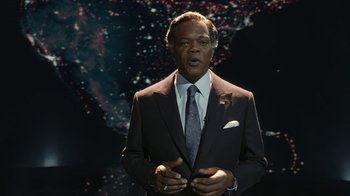 Movie still from “RoboCop” (2014), directed by José Padilha – A man in a suit and tie standing in front of a space background; Medium shot, Low angle