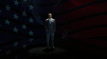 Movie still from “RoboCop” (2014), directed by José Padilha – A man in a suit standing in front of an american flag; Wide shot, Low angle