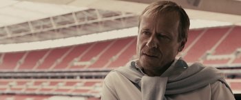 Movie still from “RocknRolla” (2008), directed by Guy Ritchie – An older man wearing a white shirt and a gray scarf; Close Up shot, Low angle