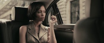 Movie still from “RocknRolla” (2008), directed by Guy Ritchie – A woman sitting in the back of a car smoking a cigarette; Close Up shot, Over the shoulder angle