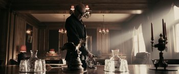 Movie still from “RocknRolla” (2008), directed by Guy Ritchie – An old man in a black suit standing in front of a table; Medium shot, Low angle