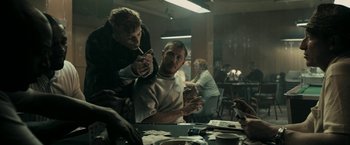 Movie still from “RocknRolla” (2008), directed by Guy Ritchie – A group of people sitting around a table; Medium shot, Over the shoulder angle
