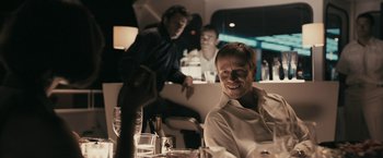 Movie still from “RocknRolla” (2008), directed by Guy Ritchie – A man sitting at a table in front of two other men; Medium shot, Over the shoulder angle