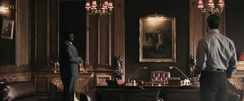 Movie still from “RocknRolla” (2008), directed by Guy Ritchie – A man standing in a living room next to a painting; Wide shot, Low angle