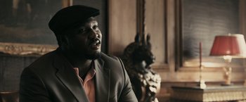Movie still from “RocknRolla” (2008), directed by Guy Ritchie – A man wearing a suit and hat looking up; Close Up shot, Low angle
