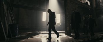 Movie still from “RocknRolla” (2008), directed by Guy Ritchie – A man in a suit walking in a dark room; Wide shot, Low angle