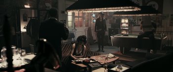 Movie still from “RocknRolla” (2008), directed by Guy Ritchie – A woman sitting on top of a couch in front of a pool table; Wide shot, Over the shoulder angle