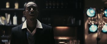 Movie still from “RocknRolla” (2008), directed by Guy Ritchie – A man wearing a suit and tie standing in a dark room; Close Up shot, Low angle