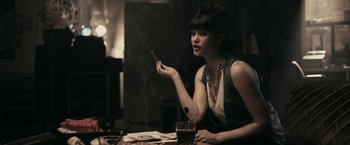 Movie still from “RocknRolla” (2008), directed by Guy Ritchie – A woman sitting at a table with a cigarette in her hand; Medium shot, Low angle