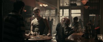 Movie still from “RocknRolla” (2008), directed by Guy Ritchie – A man sitting at a table in a room; Medium shot, Over the shoulder angle