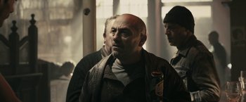 Movie still from “RocknRolla” (2008), directed by Guy Ritchie – An older man with a beard is looking into the distance; Medium shot, Over the shoulder angle