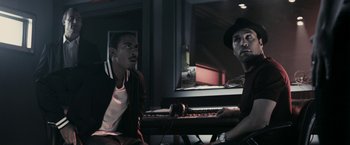 Movie still from “RocknRolla” (2008), directed by Guy Ritchie – Two men sitting in front of a keyboard in a dark room; Medium shot, High angle