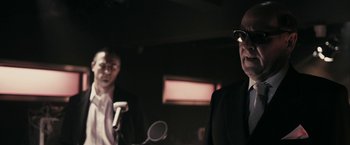 Movie still from “RocknRolla” (2008), directed by Guy Ritchie – Two men in black suits are standing in front of a microphone; Close Up shot, Low angle
