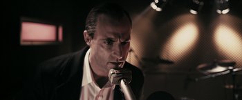 Movie still from “RocknRolla” (2008), directed by Guy Ritchie – A person holding a microphone; Close Up shot, Low angle