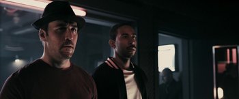 Movie still from “RocknRolla” (2008), directed by Guy Ritchie – Two men standing next to each other in front of a building; Close Up shot, Over the shoulder angle