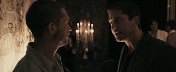 Movie still from “RocknRolla” (2008), directed by Guy Ritchie – Two men standing next to each other in front of candles; Close Up shot, Over the shoulder angle