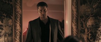 Movie still from “RocknRolla” (2008), directed by Guy Ritchie – A man standing in front of a mirror in a room; Medium shot, Over the shoulder angle