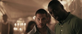 Movie still from “RocknRolla” (2008), directed by Guy Ritchie – Two men standing next to each other in front of a crowd; Close Up shot, Over the shoulder angle