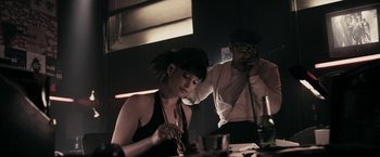Movie still from “RocknRolla” (2008), directed by Guy Ritchie – A woman sitting at a table with a man on the phone; Medium shot, Low angle