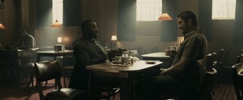 Movie still from “RocknRolla” (2008), directed by Guy Ritchie – A man sitting at a table in a restaurant; Medium shot, Over the shoulder angle